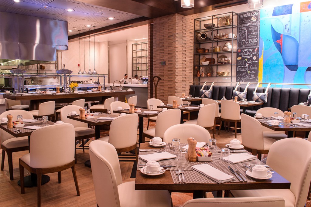 Mesas de madera juegan con sillas blancas y sillones negros con cojines tipo booth, realizados por Humberto Ramirez, de HR Muebles. En la pared, pizarra a la usanza de las plazas de mercado.