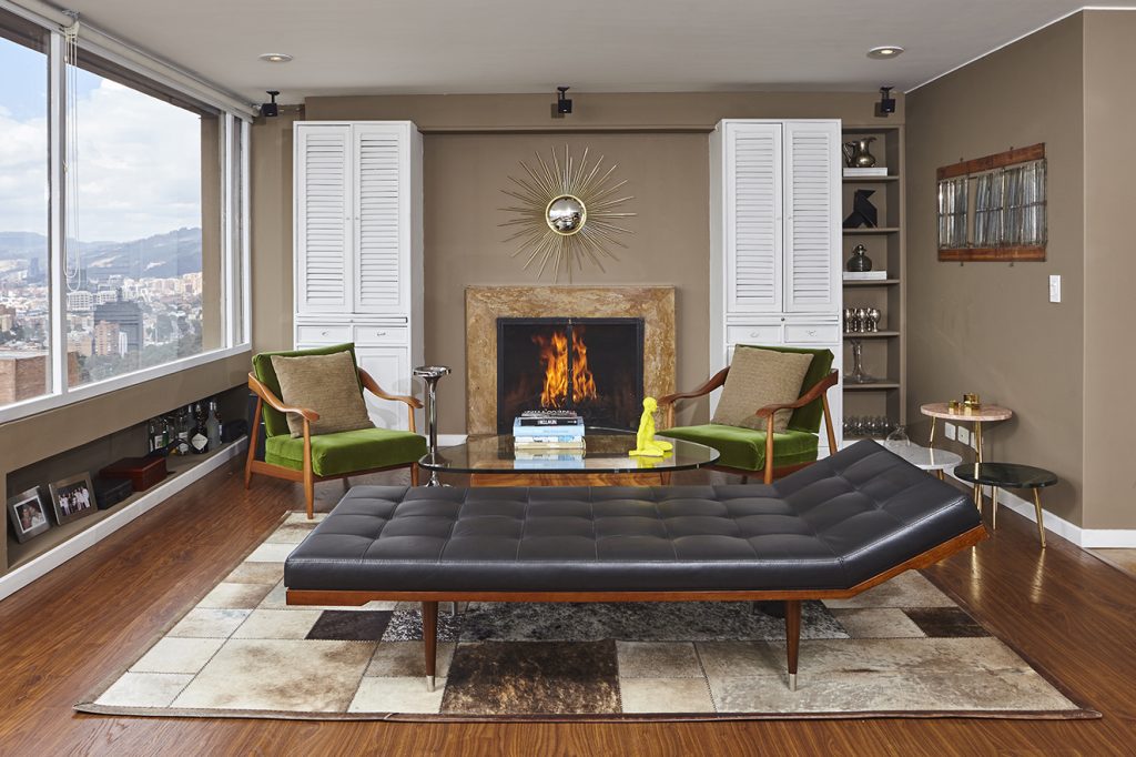 Las mezclas siguen vigentes, como en esta sala que incluye el chaise longue modernista, de cuero negro, diseño de ELECEmobiliario; dos poltronas danesas de los años cincuenta tapizadas con terciopelo verde oliva; espejo de bronce 'Sol' con luneta ojo de pez, fabricado por Manos Artesanas; y las mesas auxiliares ‘Gabriela’ de bronce y mármol. Todo de Folies. Fotografía: cortesía Folies.