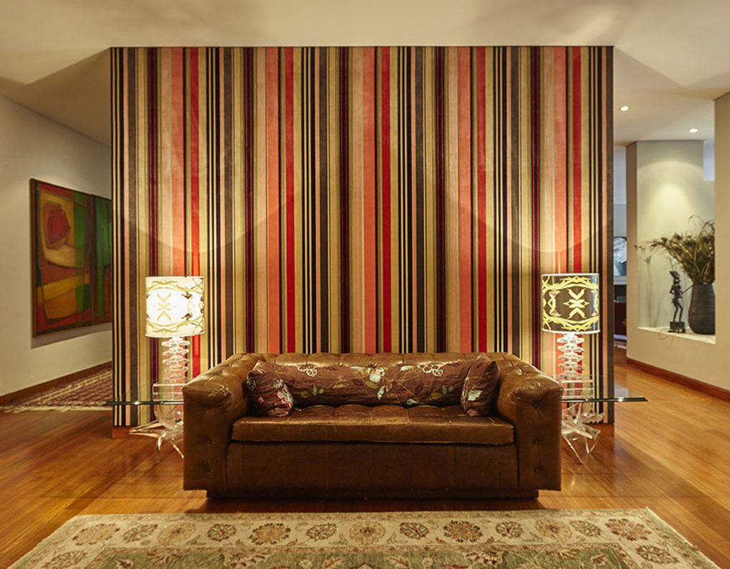 En el hall de entrada, pared cubierta con tela de Kenzo, comprada en Michel Editores; sofá de cuero estilo inglés, herencia de familia; dos mesitas del anticuario Cinco en Punto; y tapete traído de la India. A la derecha se aprecia el nicho que se generó al eliminar parte del muro entre el corredor y el comedor. Fotografía: Gabriel Lugo.