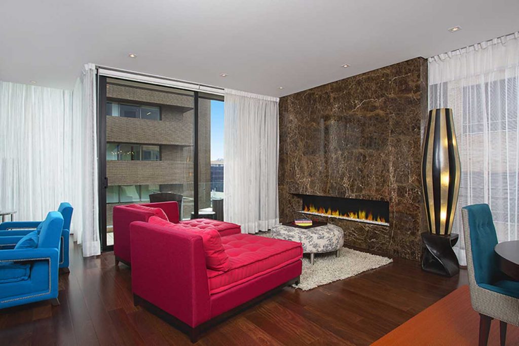Un llamativo elemento de diseño es la pared recubierta con mármol que alberga la chimenea de gas. El tapete de fieltro es de Mesas&Sillas. Los velos de las cortinas son de malla de Maritel del Nogal. Fotografía: Luis Fernando Ramos.