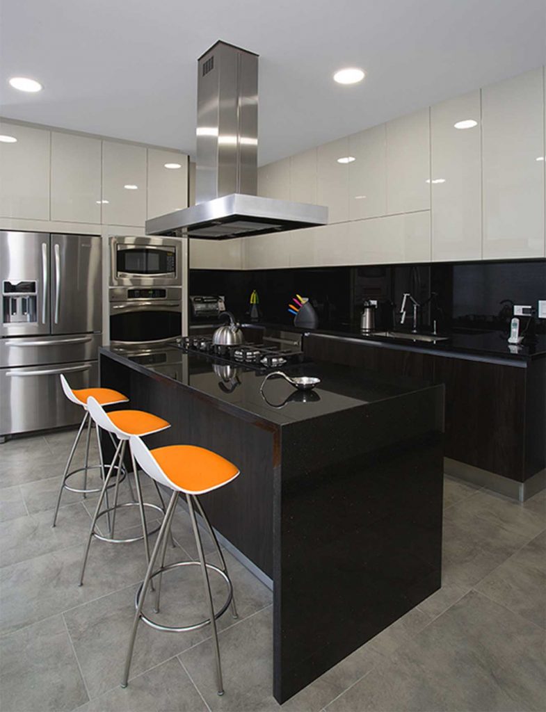 Cocina con isla con mesón de granito ‘negro estelar’. Los muebles inferiores son de melamina negra y los superiores, de poliuretano gris hielo. Para contrastar se instaló porcelanato gris en el piso. El toque de color lo dan las bancas de Mesas&Sillas. Fotografía: Luis Fernando Ramos.