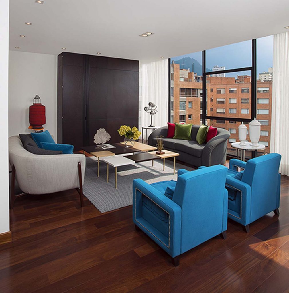 Para la sala principal la diseñadora creó poltronas y sofás tapizados con paños de diferentes colores, y cojines de terciopelo, todo con telas de Michel Editores. Las mesas son de madera con tres acabados y patas de bronce. Al fondo, lámpara vintage de Dessvan.