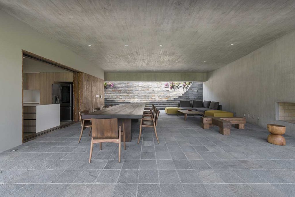 Para el piso del área social se escogió piedra gris en formato cuadrado que juega con el techo y paredes de concreto a la vista. Muebles de madera maciza tanto para el comedor como en la sala  visten el espacio que sorprende por su austeridad. La arquitectura habla por sí sola. Fotografía: Renzo Rebagliati.