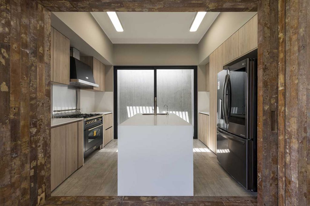 Puertas corredizas de madera rústica permiten abrir la cocina al a´rea social. Se destaca el diseño con isla para mayor funcionalidad y aprovechamiento del espacio. Fotografía: Renzo Rebagliati.