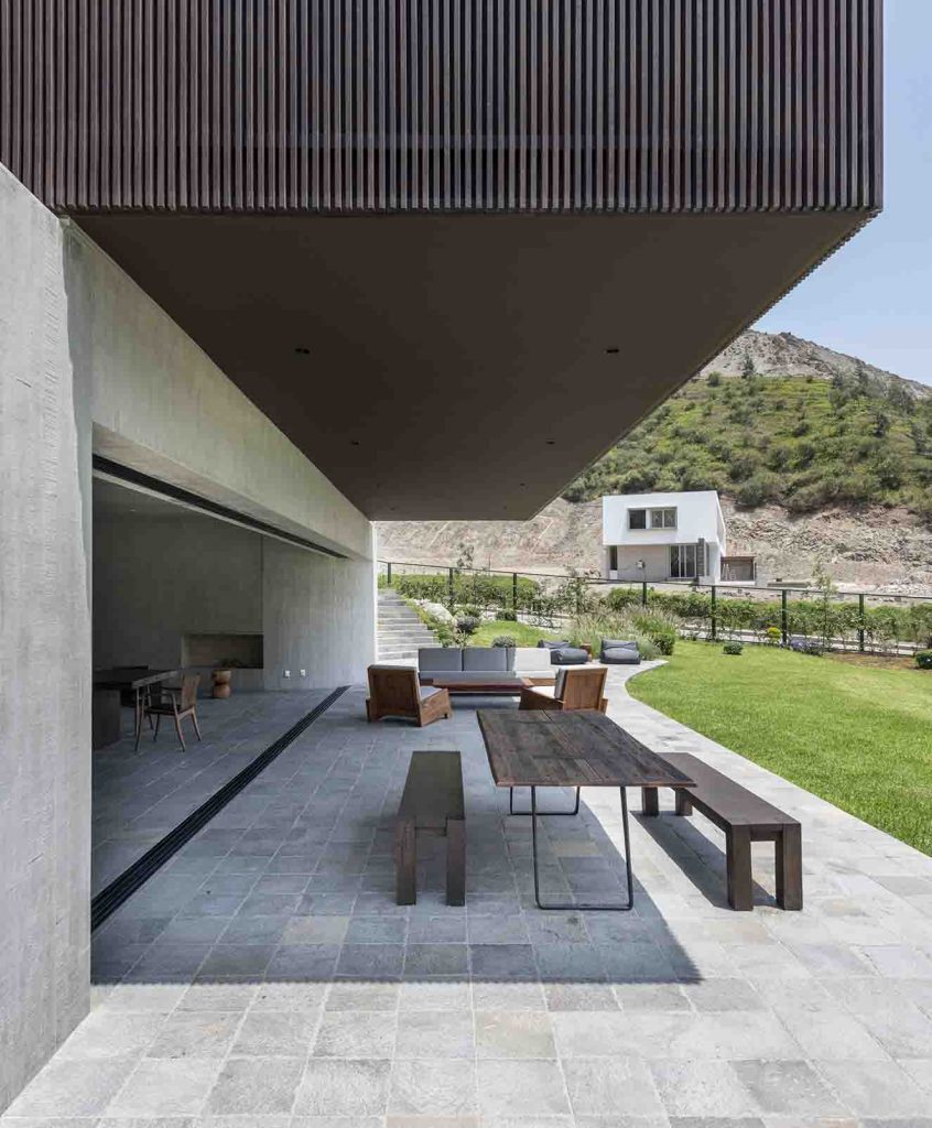Puertas corredizas permiten abrir completamente el a´rea social a la terraza, creando un solo gran ambiente. Una mesa de madera rústica con dos bancas y una sala también de madera y lona banca conforman el austero amoldamiento de la terraza. Fotografía: Renzo Rebagliati. 