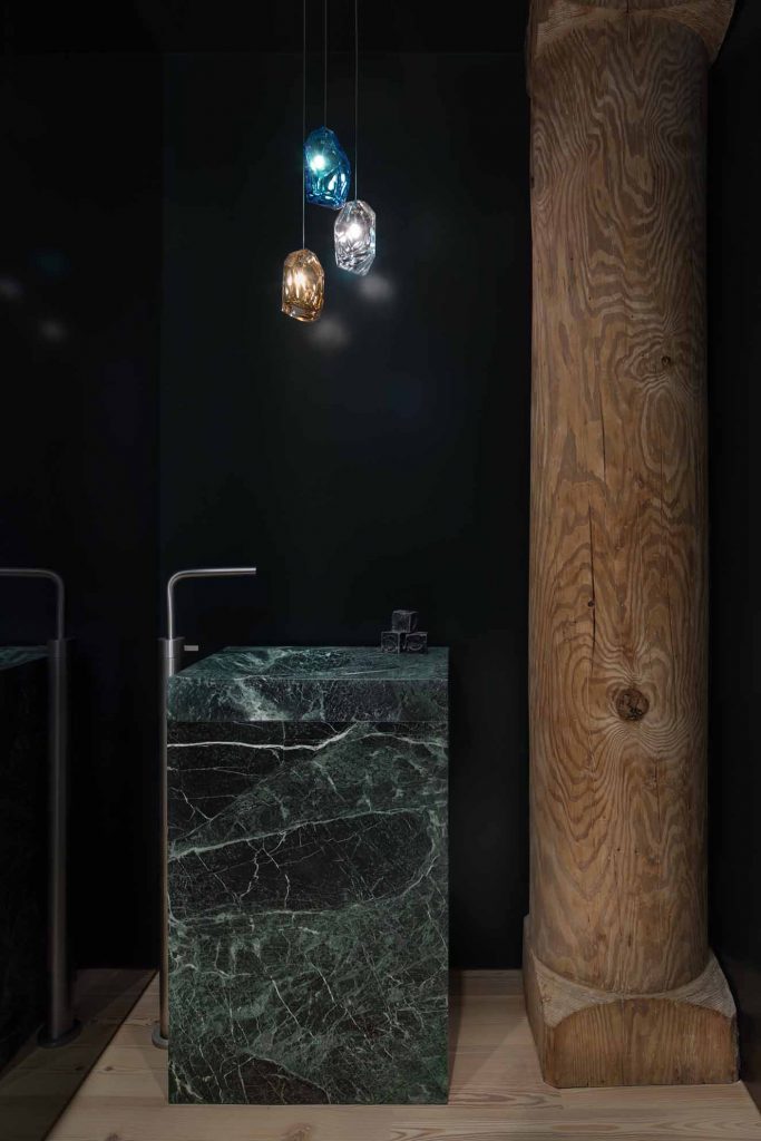 El baño social contiene una pared de vidrio ahumado que refleja un lavamanos de mármol Tinos Green hecho a la medida y una antigua columna de madera. Fotografía: Eric Petschek, cortesía Worrel Yeung.